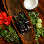Two bottles of olive oil on a wooden surface with herbs and a red flower.