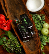 Two bottles of olive oil on a wooden surface with herbs and a red flower.