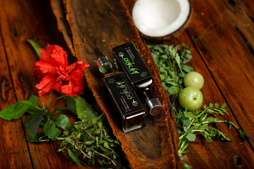 Two bottles of olive oil on a wooden surface with herbs and a red flower.